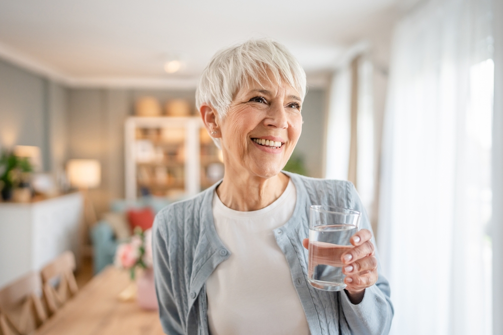 Smiling senior woman holding glass of water after successful Periodontics treatment at Craft Dental