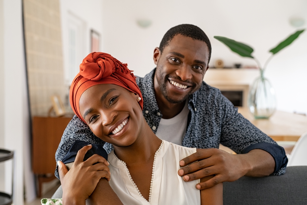 Smiling woman in a red head wrap embraced by a smiling man